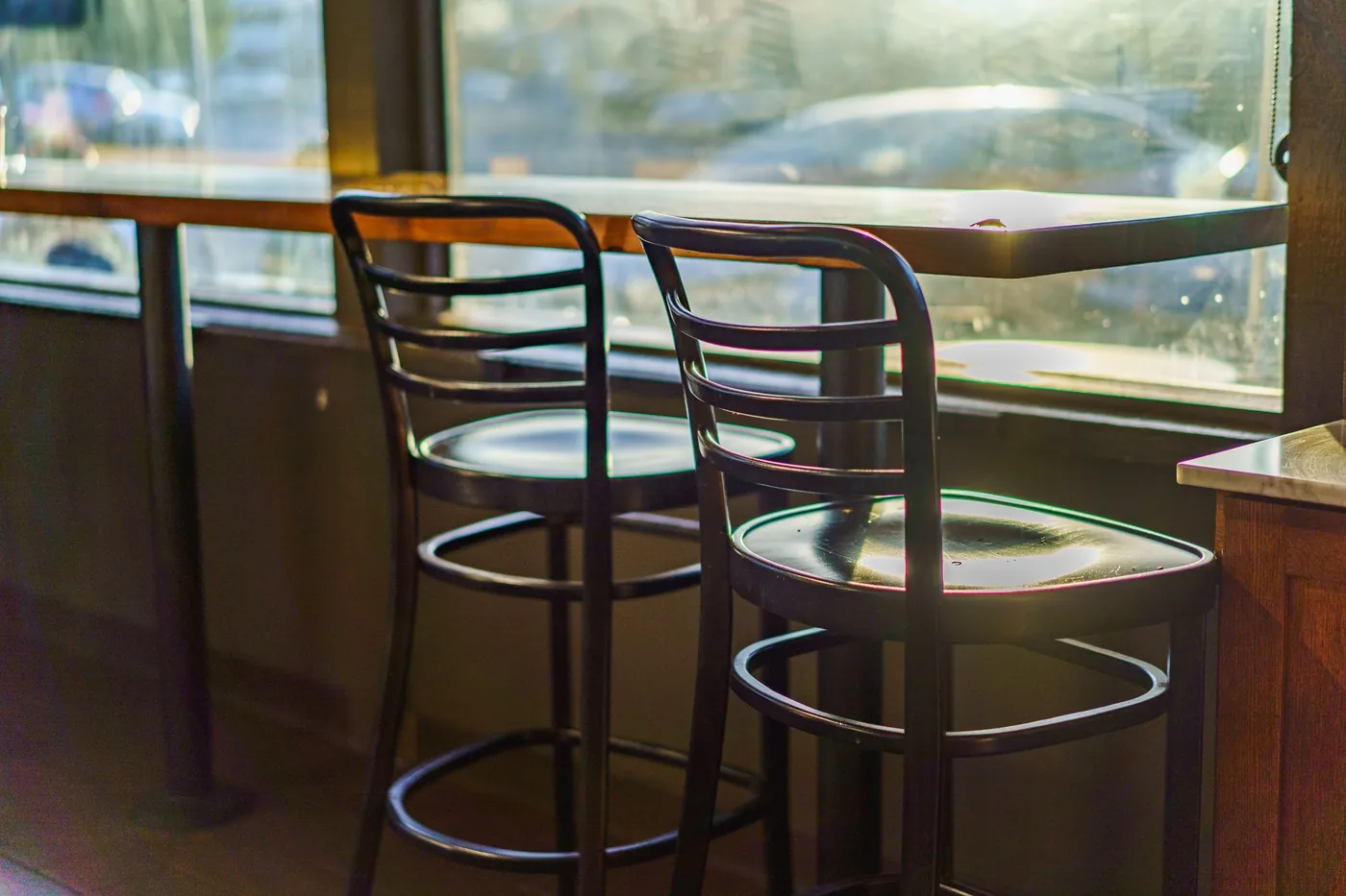 Sunlit cafe window with two empty chairs at a wooden counter